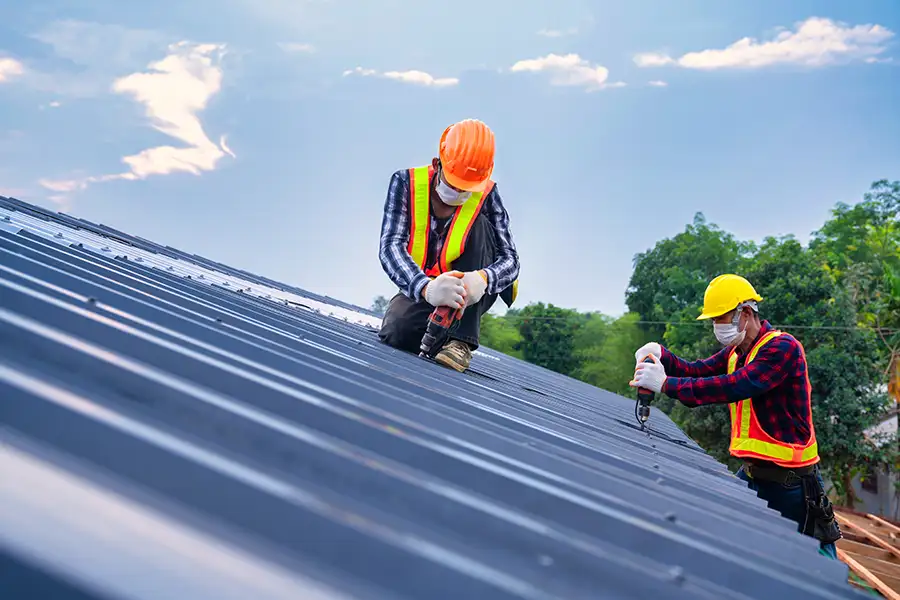 Roofers using drilling tool to install an energy-efficient metal roof on the home of a Central, IL resident.