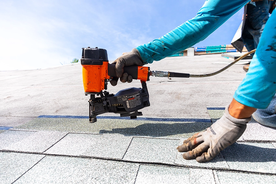 Roofer in Central IL using a tool to install new shingles for a re-roofing project for a homeowner.