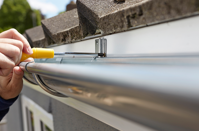 worker installing or repairing a new metal rain gutter on a house roof central il